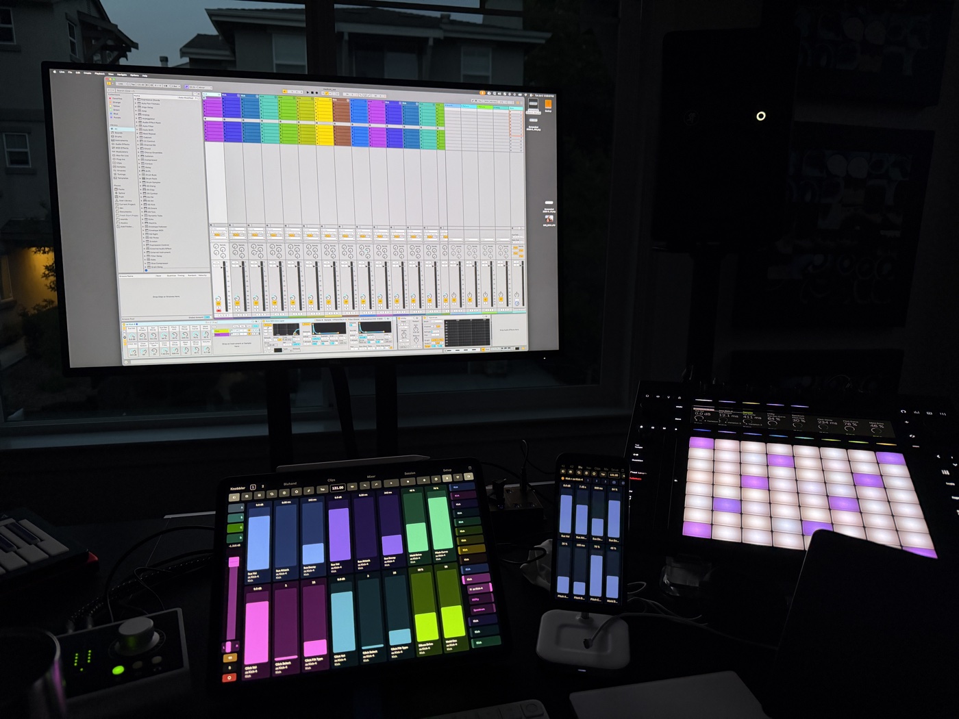 Studio desk at dusk: Ableton Live Session view on the monitor, with the Knobbler mixer running on both an iPad and a phone below it, beside glowing Push pads.